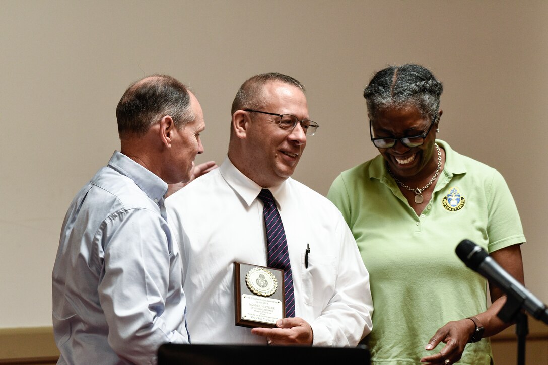 U.S. Army Maj. Sharon Browne, 7th Transportation Brigade (Expeditionary) brigade chaplain, presents Master Sgt. Neil Hertzler, XVIII Airborne Corps chaplain, with a plaque for his work as the devotional speaker during the 244th Chaplain Corps Anniversary celebration event in Williamsburg, Virginia, July 26, 2019.