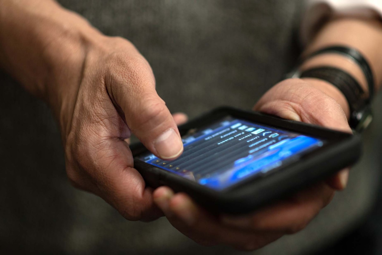 A man’s hands typing on a cellphone. The contents on the screen are undeterminable.