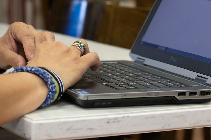 Hands typing on a laptop computer at a white table.