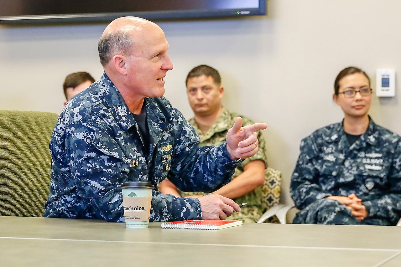 An admiral points as he speaks with sailors.