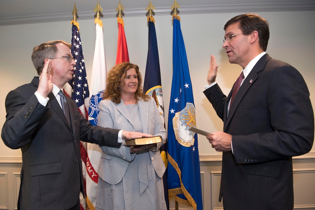 Two men hold their right hands facing each other while a woman stands in between holding a Bible.