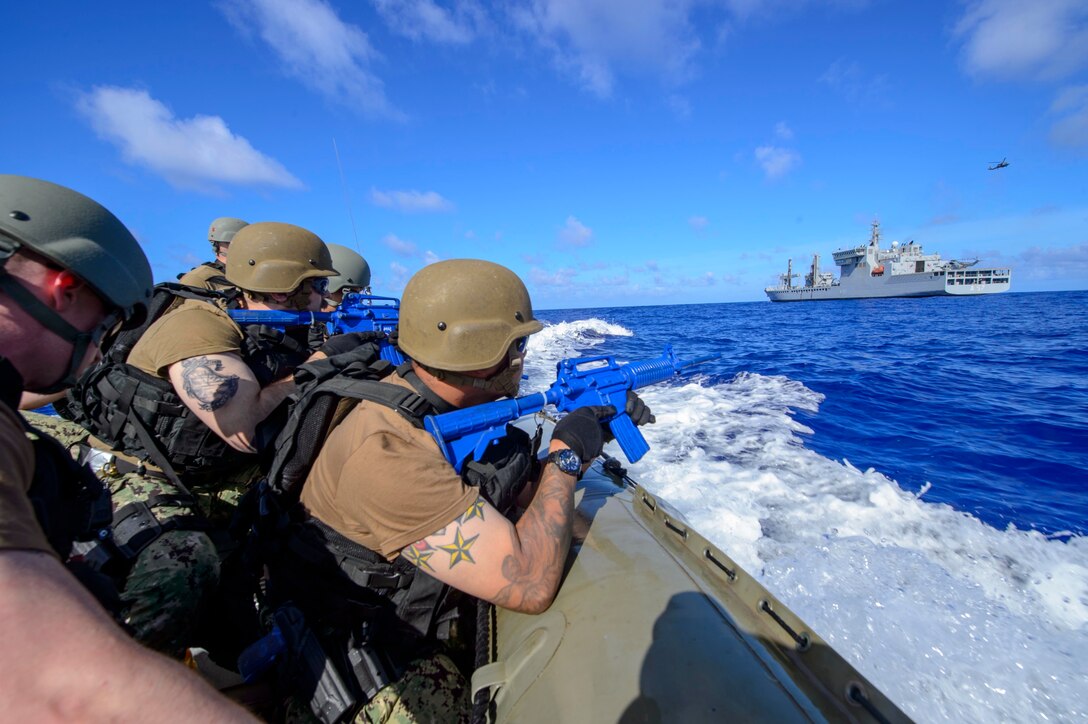 Armed military personnel in a small boat approach a larger military vessel.