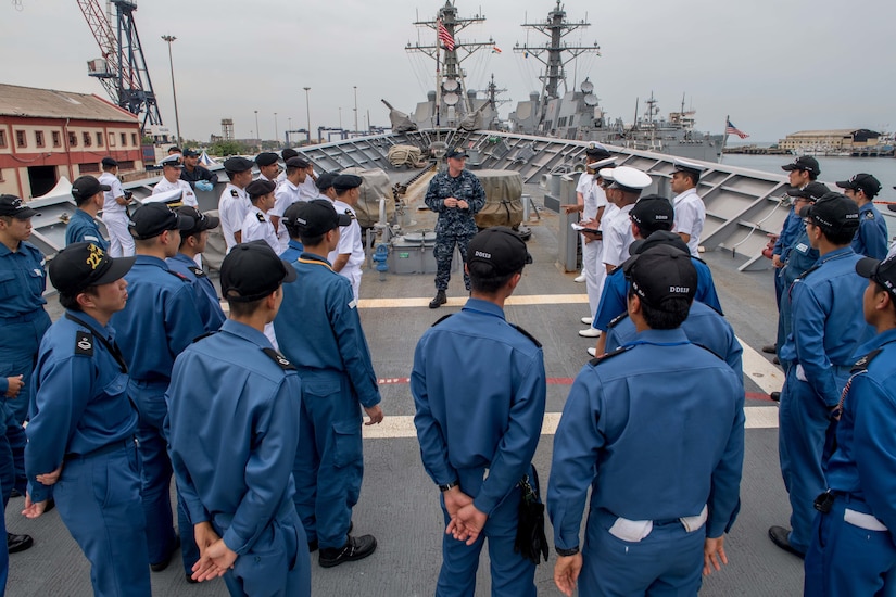 Military personnel gather around a U.S. sailor on the deck of a military vessel.