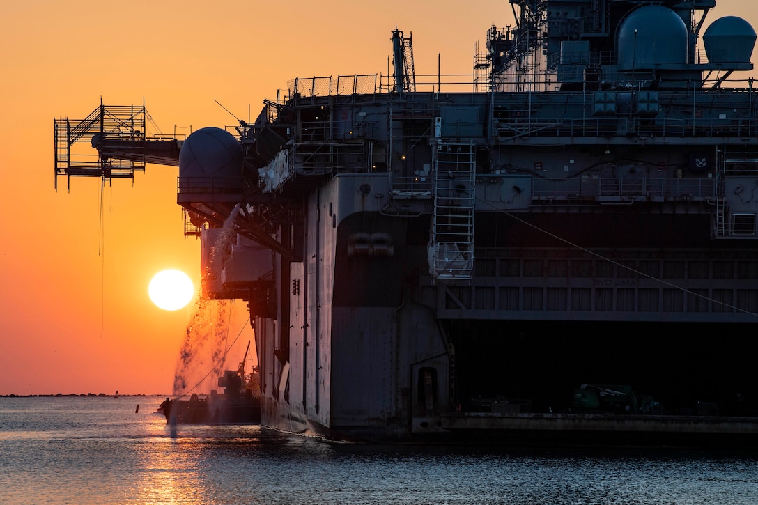 The sun hangs low in the sky over a Navy ship in homeport.