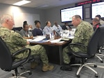 Group of men and women talking to each other while sitting at a table.