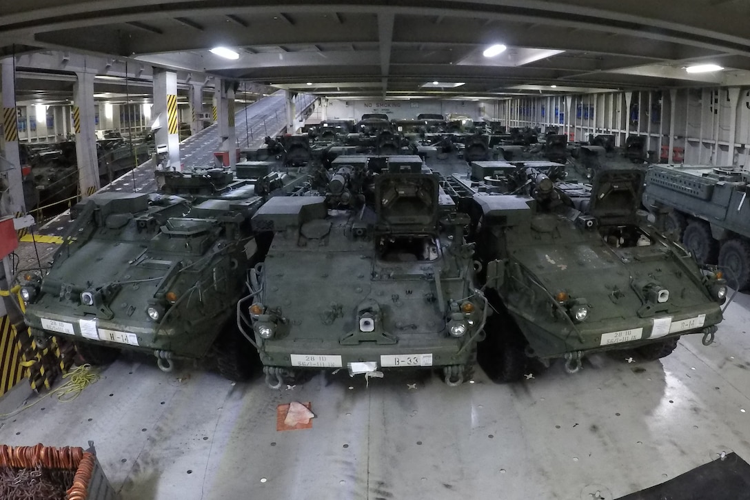 Armored vehicles sit in the hold of a ship.