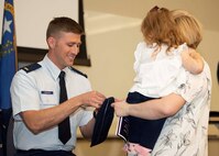 An Airman pins on 2nd Lieutenant  to his cover alongside his wife and child.