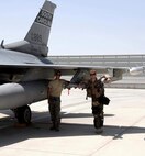 Two Airmen stand  under the wing of an F-16 Fighting Falcon fighter jet.