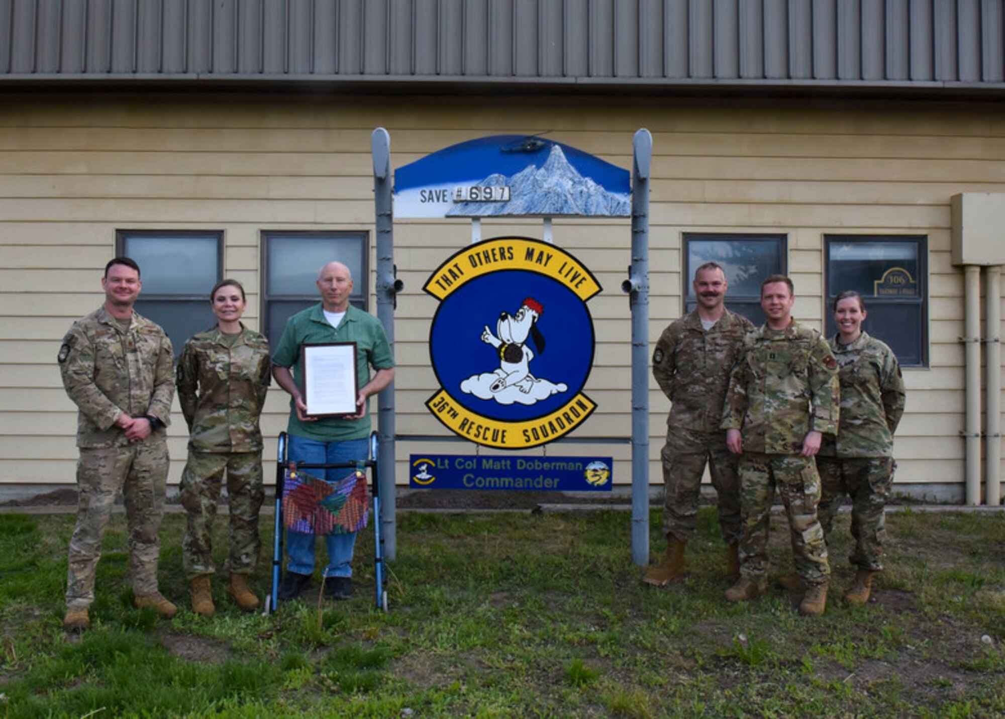Karl Shoemaker and Airmen from the 36th Rescue Squadron and Survival, Evasion, Resistance and Escape, pose for a photo in front of the 36th RQS sign on Fairchild Air Force Base, Washington, May 22, 2019. The number on the sign represents how many lives the 36th RQS has saved; Shoemaker was number 697. (U.S. Air Force photo by Airman Kiaundra Miller)
