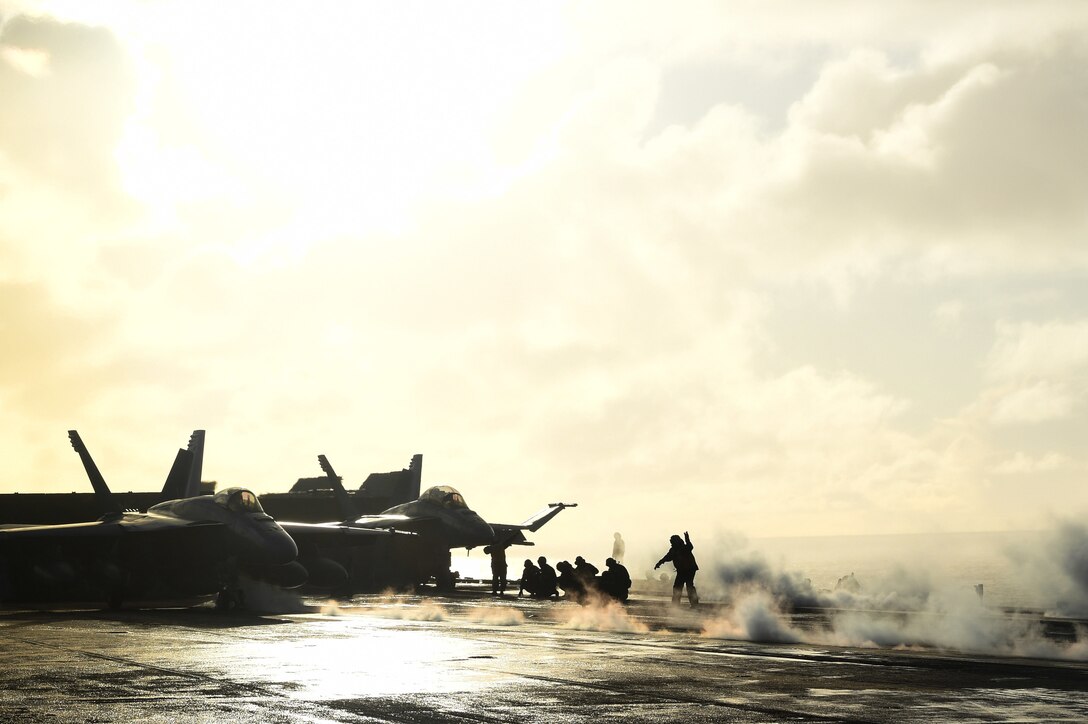 Steam surrounds jets on a carrier deck.