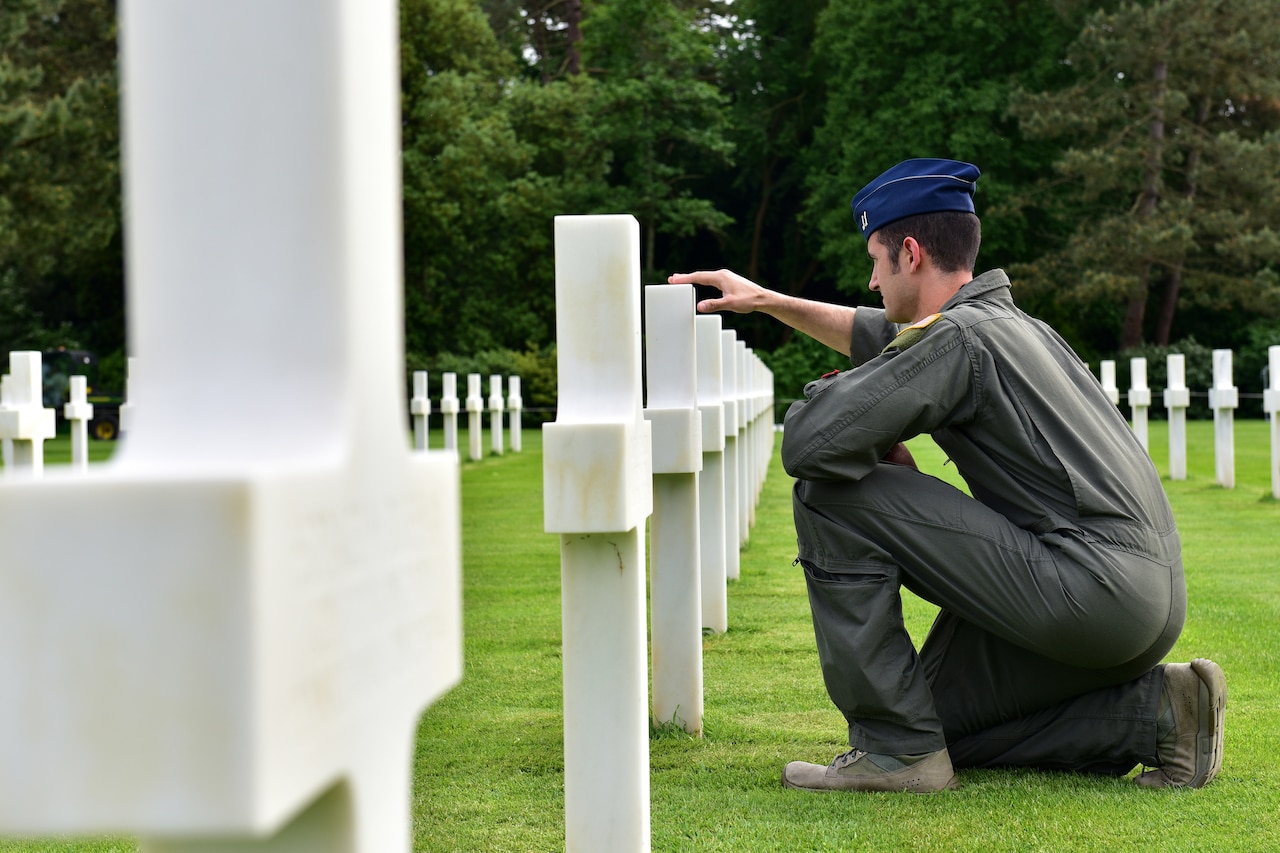 An airman kneels before a tombstone in a cemetery.