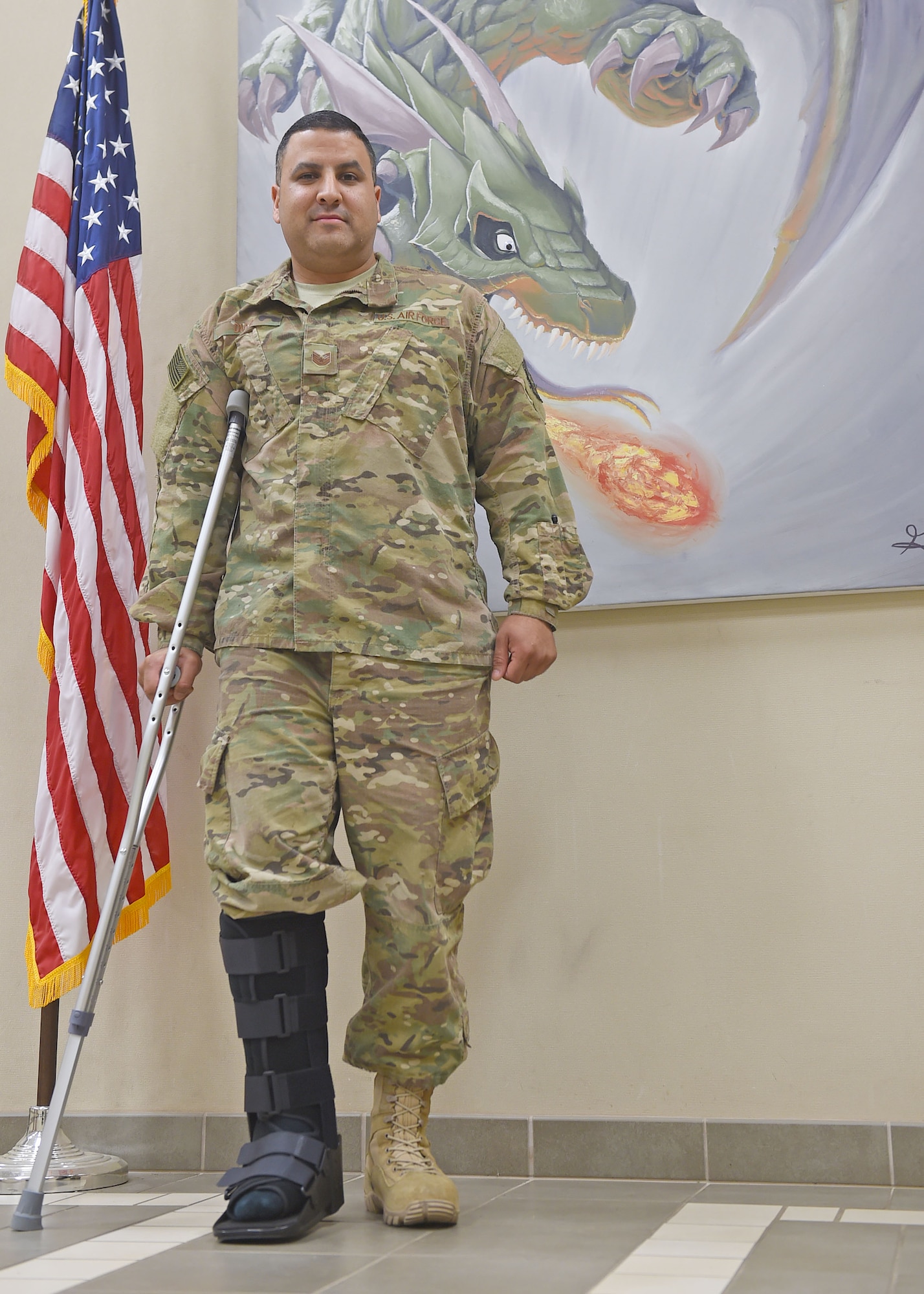 An Airman with a cast on his foot poses for a photo in front of an American flag