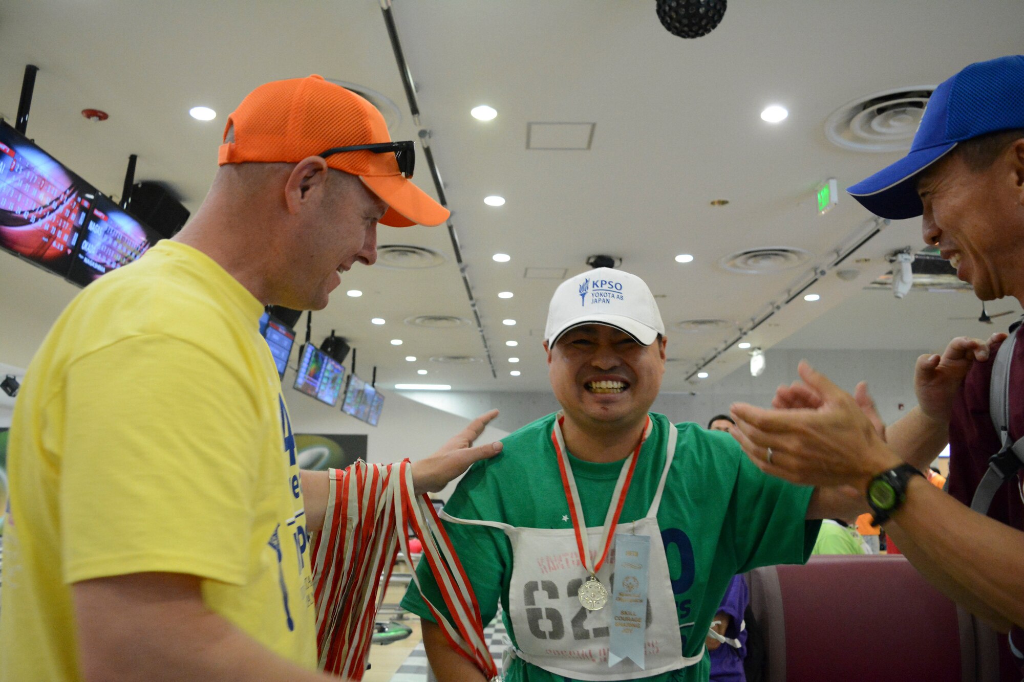 An Athlete celebrates receiving a medal with the medal presenter and his buddy during the medal ceremony of the bowling competition during the 40th Annual Kanto Plains Special Olympics at Yokota Air Base Japan, June 1, 2019.
