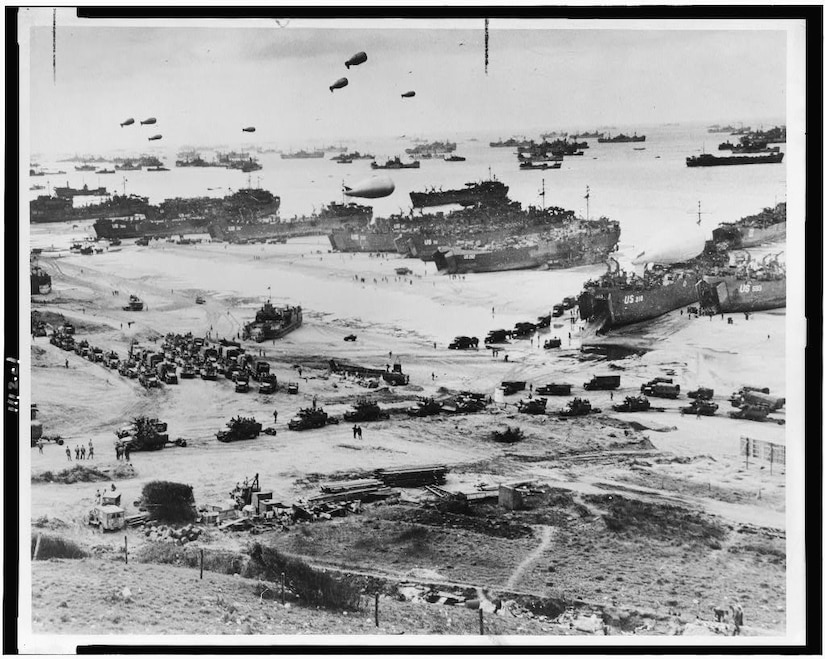 A bird’s-eye view of a beach covered in landing craft, tanks and soldiers.