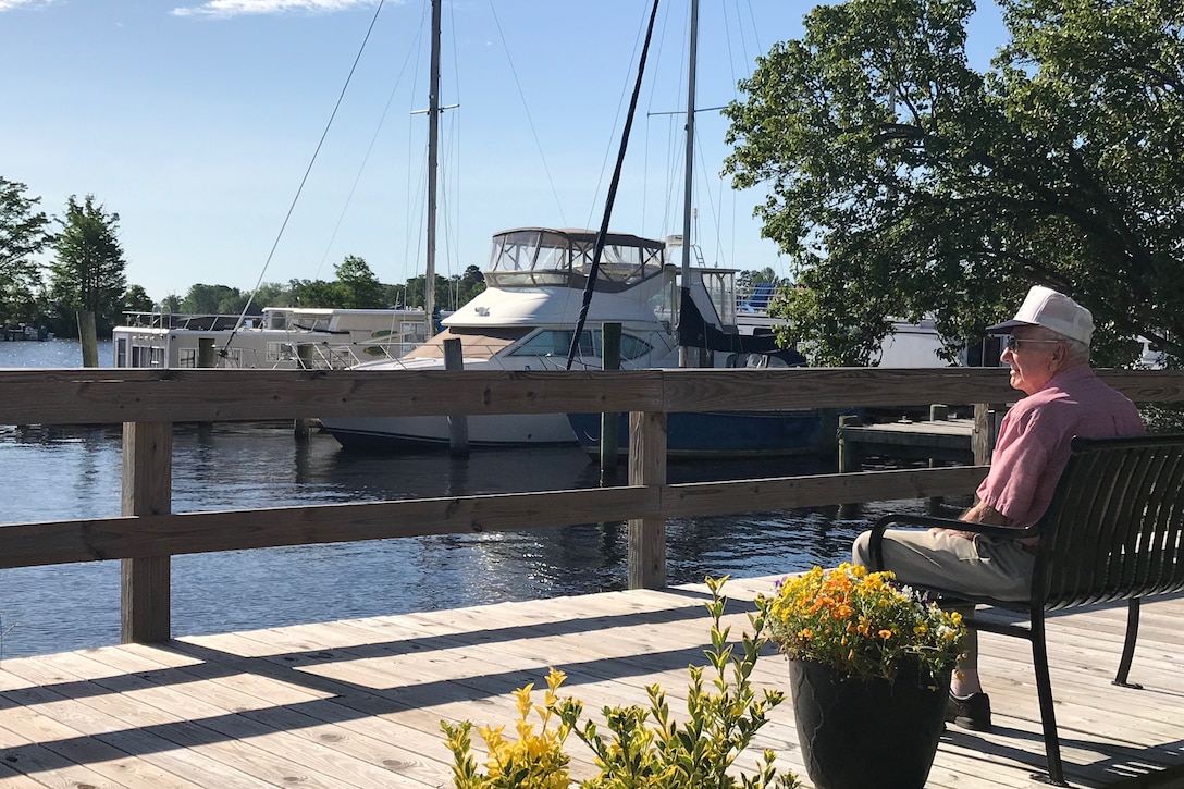 A World War II vets sits on a bench beside a boat marina.