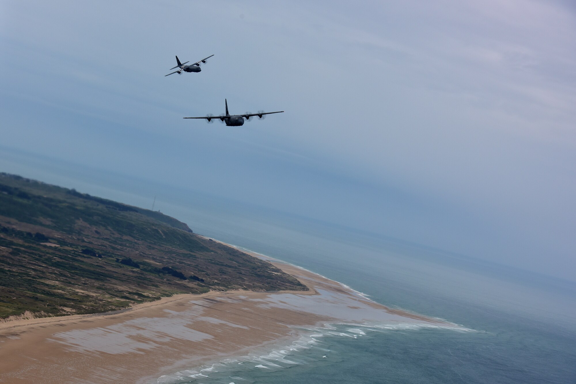 Two C-130s fly in the air over the beaches of Normandy