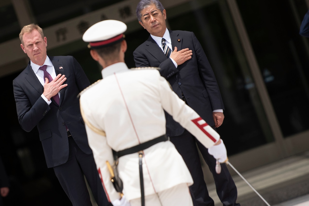 Two officials hold their hands over their hearts during an honor guard ceremony