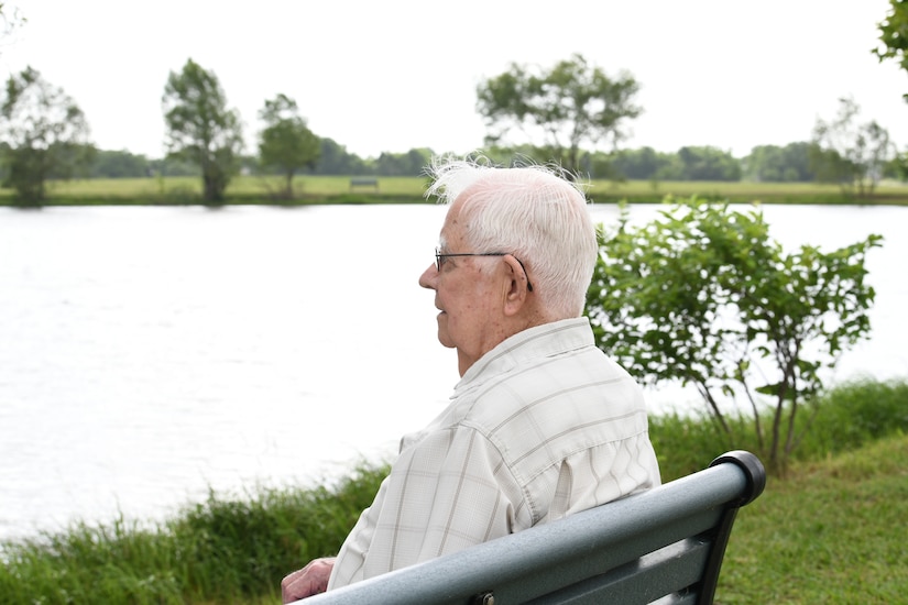 A World War II veteran sits on a bench by a lake.