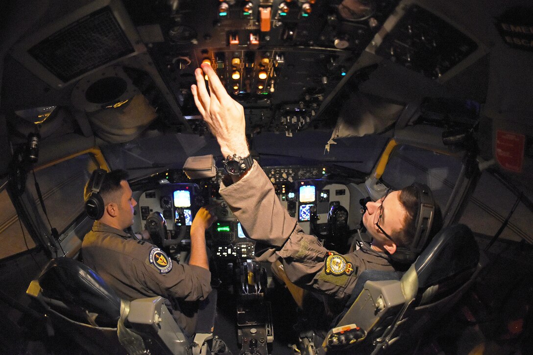 Airmen reach for controls in a cockpit.