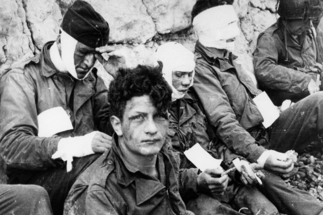 Soldiers wearing bandages sit against cliffs.