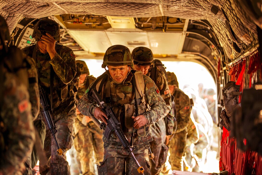 Military personnel carrying rifles enter the back of a helicopter.
