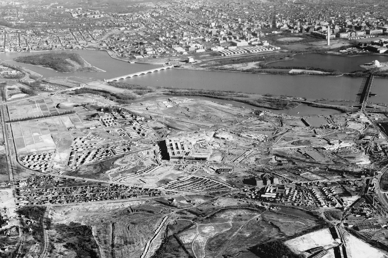 An aerial view of two sides of the Pentagon that are nearly complete during its construction. The Washington Monument and Potomac River are visible in the distance.