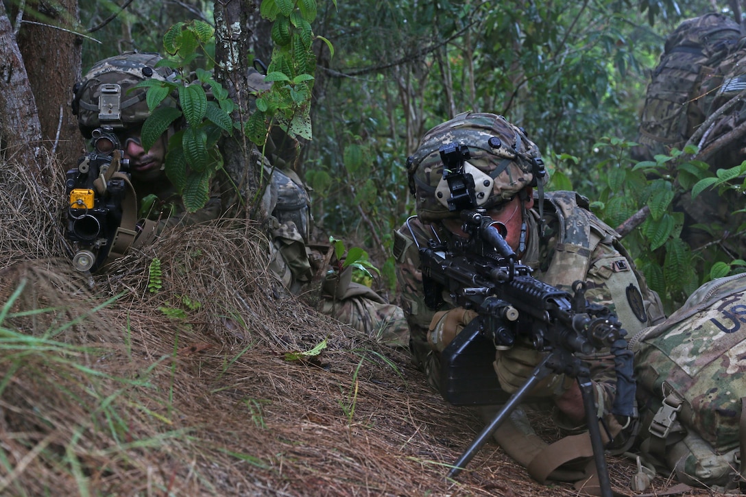 Two soldiers in a wooded area aim rifles.