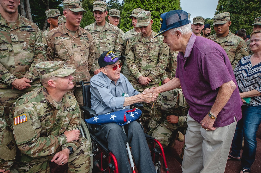 Two veterans shake hands, as soldiers crowd around them.
