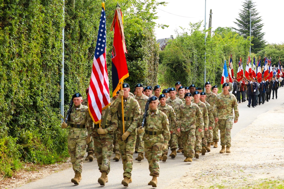 A group of soldiers march down a street some carrying flags.