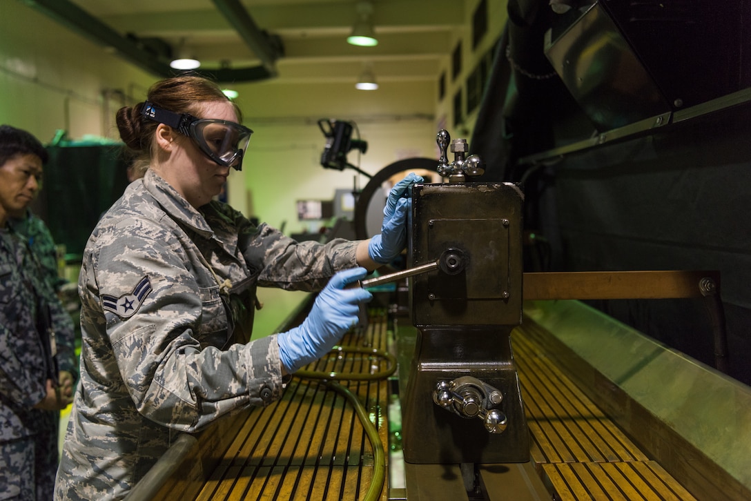U.S. Air Force Airman 1st Class Jasmyn Yoder, nondestructive inspection apprentice assigned to the 18th Equipment Maintenance Squadron, demonstrates how to use the stationary magnetic particle inspection unit during a bilateral training exercise with the Japan Air Self-Defense Force May 23, 2019, on Kadena Air Base, Japan. This bilateral training exercise focused on teaching JASDF members the functions and purpose of aerospace ground equipment and nondestructive inspection flights. (U.S. Air Force photo by Airman 1st Class Cynthia Belío)