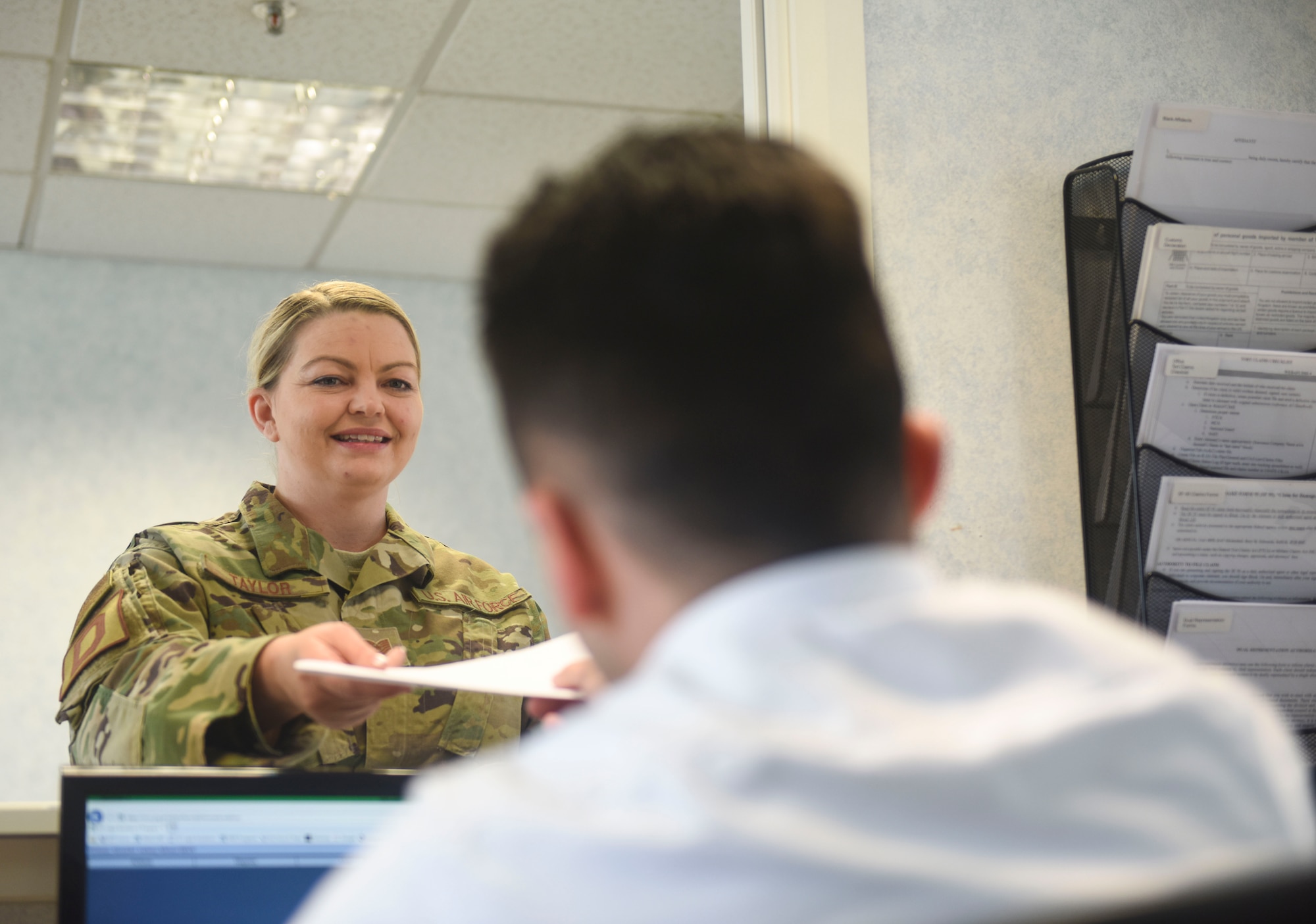 U.S. Air Force Tech. Sgt. Devan Taylor, 100th Air Refueling Wing judge advocate NCO-in-charge of general law, hands paperwork to Alex Shaw, legal assistant, at the base legal office at RAF Mildenhall, England, May 24, 2019. The base legal office has saved Airmen and families $93,200 in services like power of attorneys, notaries, wills and legal assistance in 2019. (U.S. Air Force photo by Airman 1st Class Joseph Barron)