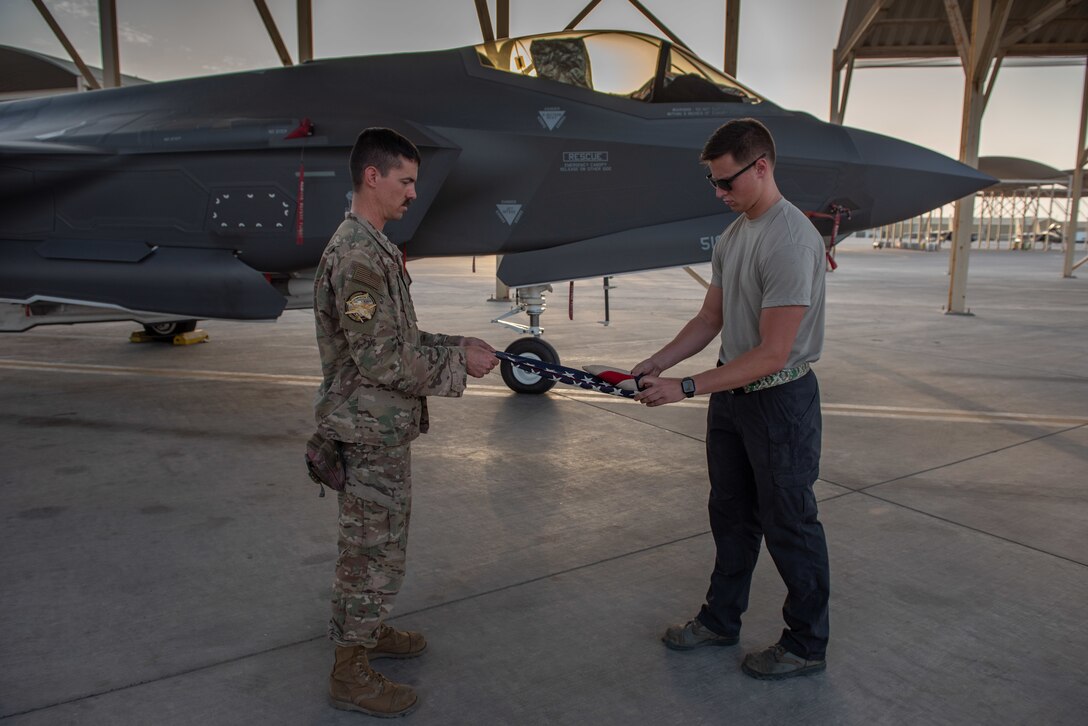 Senior Airman Quinton Bullock, right, 380th Expeditionary Aircraft Maintenance Squadron F-35A Lightning II crew chief, folds a 48-star flag June 6, 2019, at Al Dhafra Air Base, United Arab Emirates.