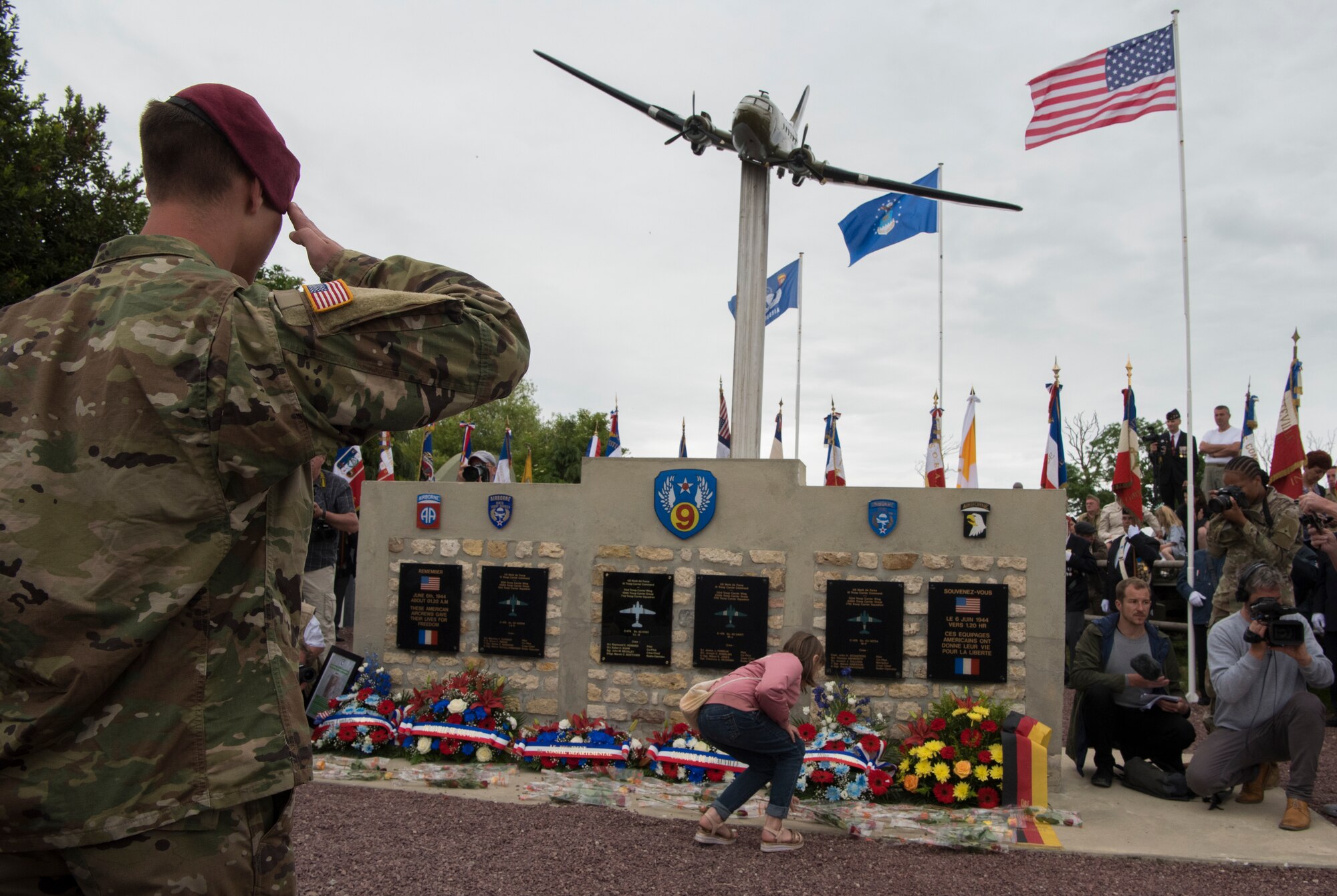 A U.S. Army airborne infantryman salutes the U.S. Air Force monument while a French child places a flower near the monument during a ceremony honoring all airborne troops and flight crew that served on D-Day in Picauville, France, June 4, 2019. Both acts honored those that paid the ultimate sacrifice on D-Day, 75 years ago. (U.S. Air Force photo by Senior Airman Kristof J. Rixmann)