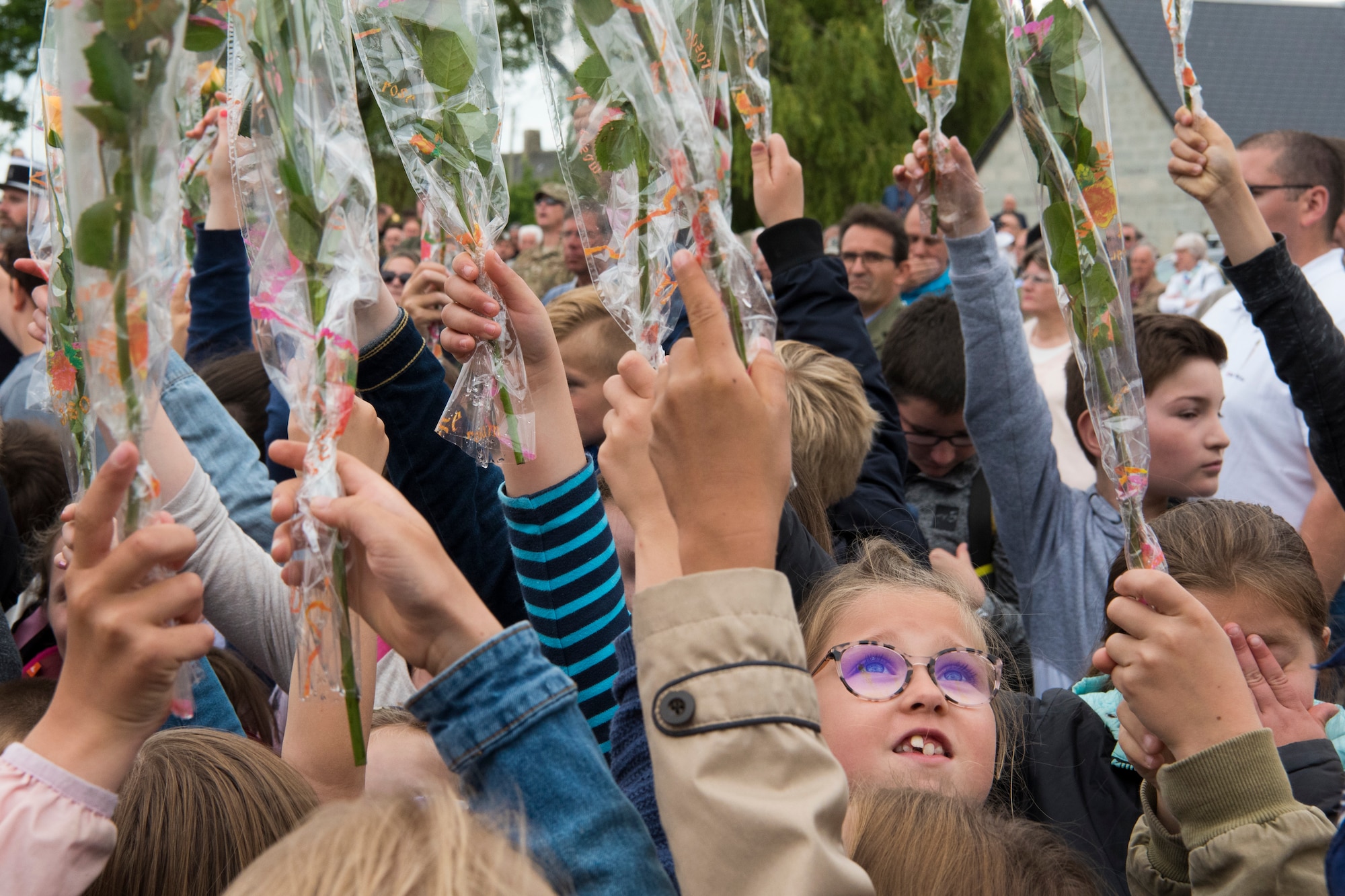 A French child looks up at the many flowers raised above the heads of her peers during a ceremony honoring all airborne troops and flight crew that served on D-Day in Picauville, France, June 4, 2019. Each child, soon after, paired up with a U.S. Army airborne infantryman as they walked together, hands held, up to the U.S. Air Force monument where the child placed their flower at the base of the monument while their soldier held a salute; both honoring those who paid the ultimate sacrifice on D-Day. (U.S. Air Force photo by Senior Airman Kristof J. Rixmann)