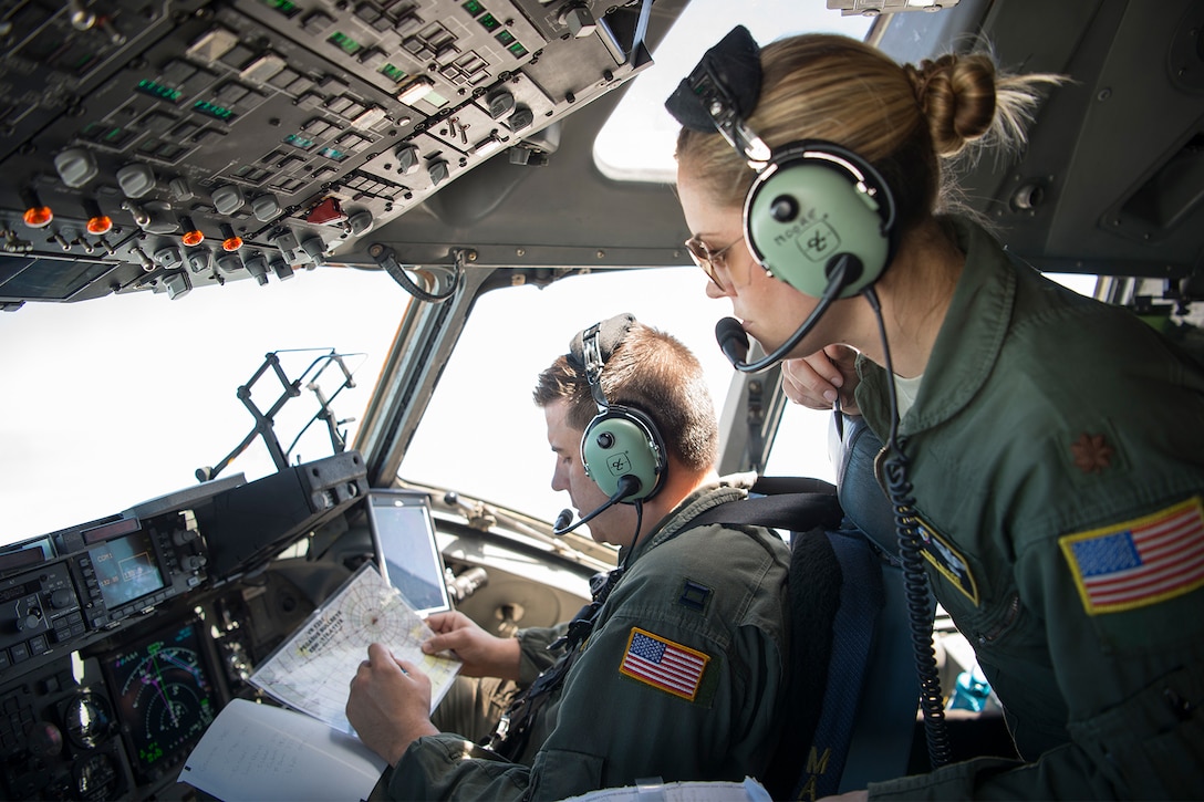 Airmen look over a map in a cockpit.