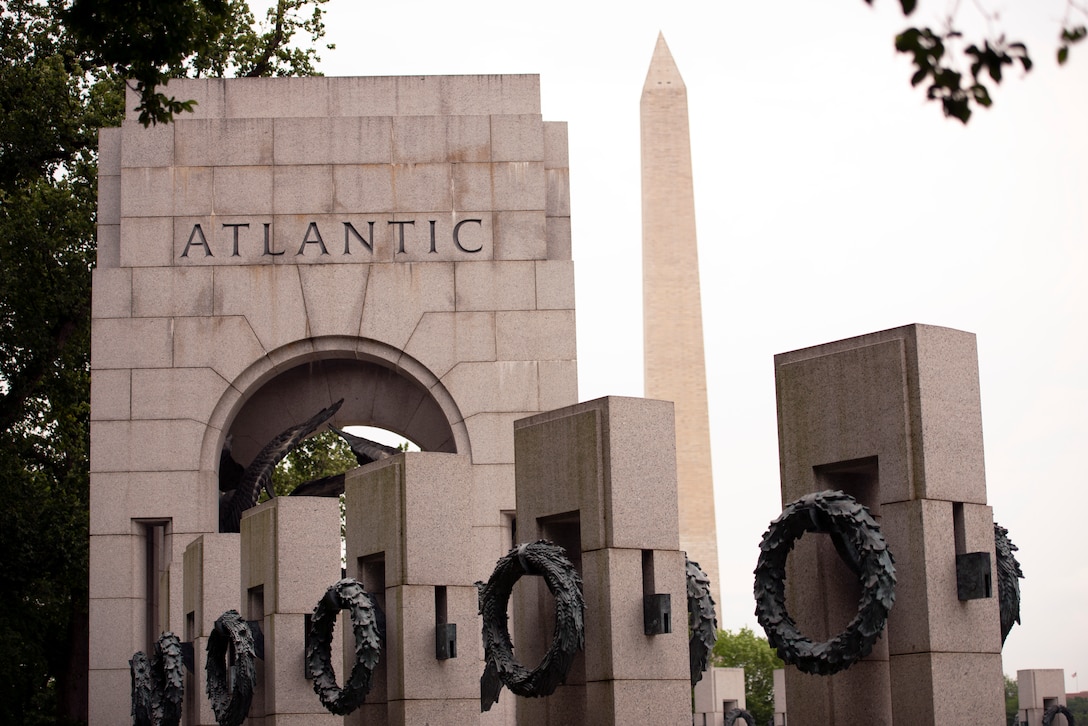 A stone arch bears the word “Atlantic.” In the background looms the Washington Monument.  In the foreground are individual pillars with bronze wreaths.