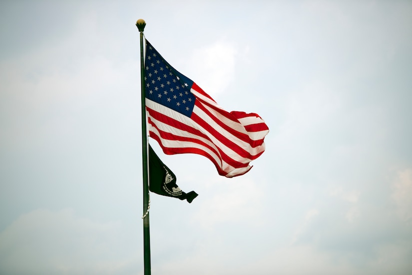 U.S. and POW/MIA flags fly against a cloudy, gray sky.