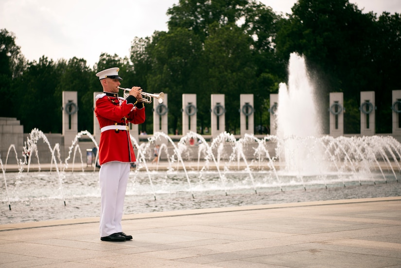 A service member in a red uniform holds a bugle to his lips.