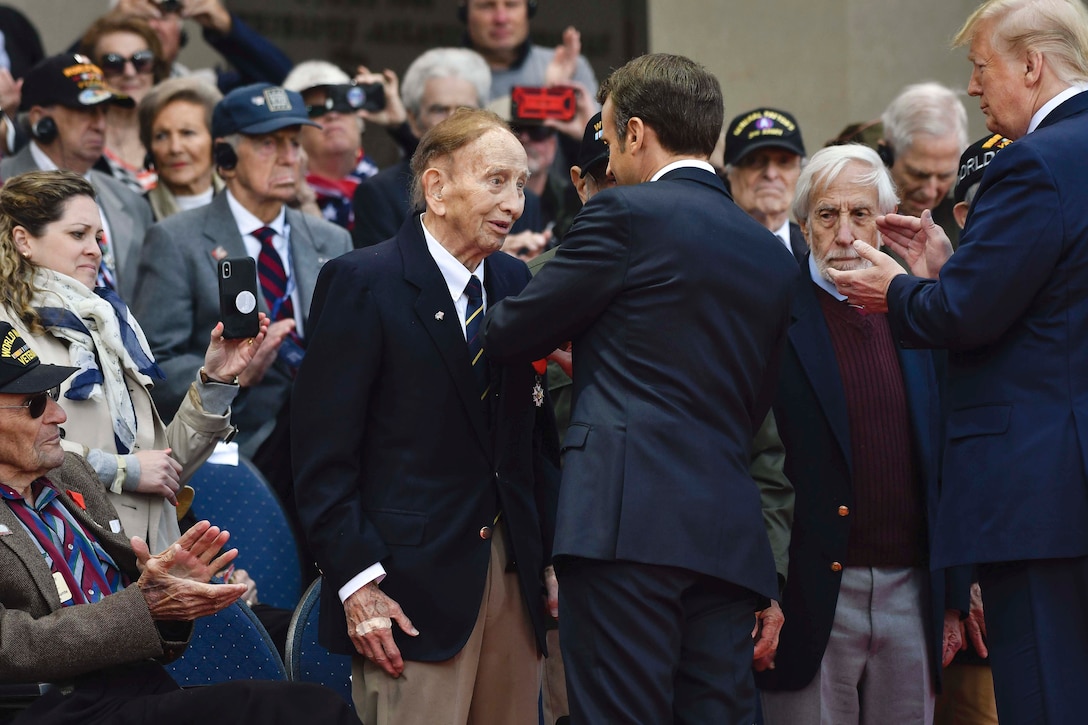 French President Emmanuel Macron gives an award to a vet as President Donald J. Trump applauds.