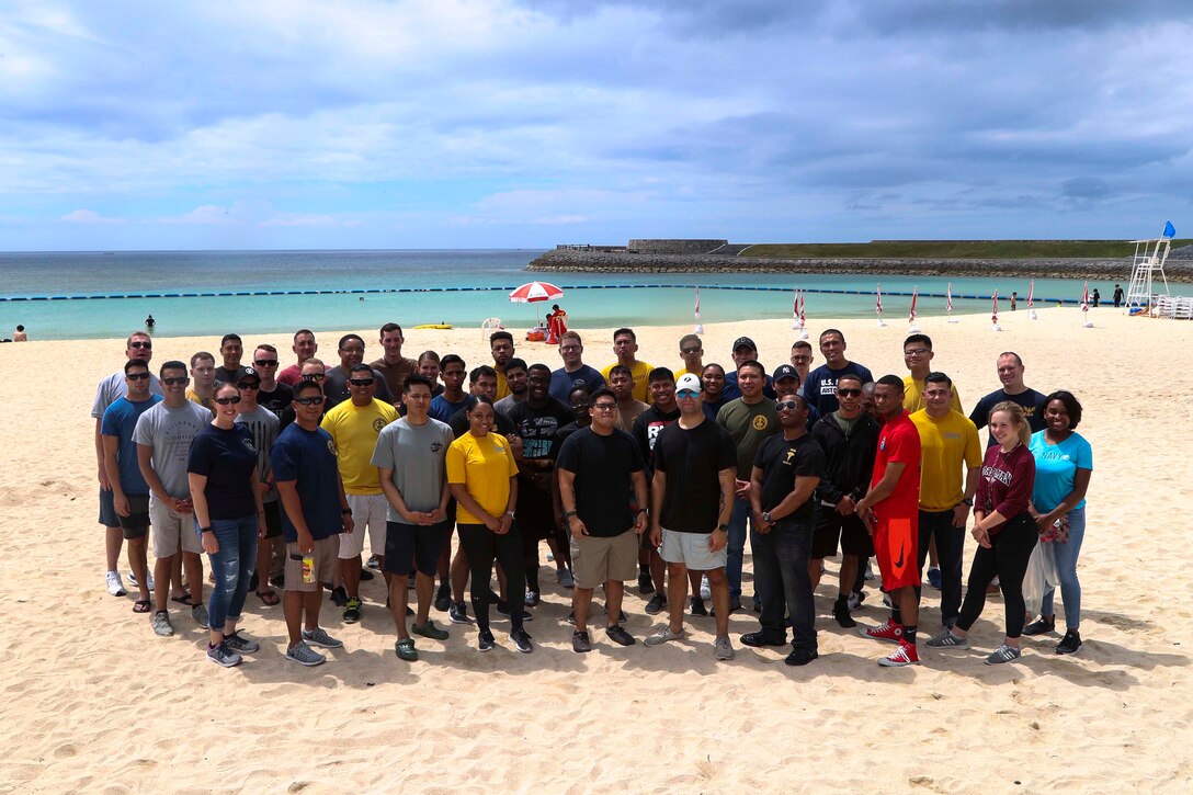 沖縄県宜野湾市にあるトロピカルビーチで清掃活動を行った在日米海兵隊所属の隊員やその家族の集合写真。第３歯科大隊の隊員とその家族が金曜日、トロピカルビーチで清掃活動を行いました。