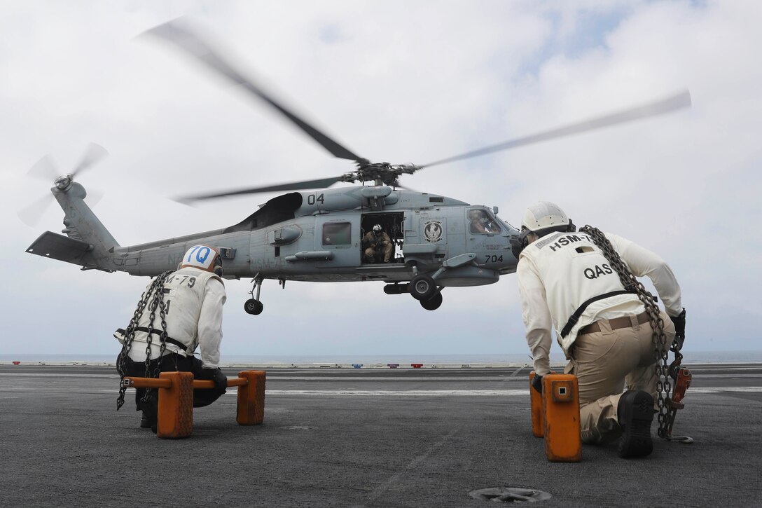 Two men crouch as a helicopter lands on a ship.