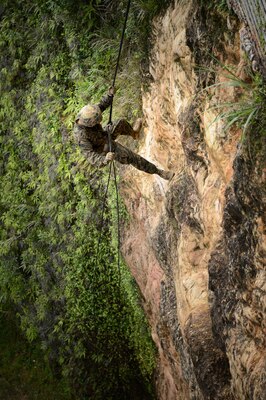 A sailor repels down a large rock face.