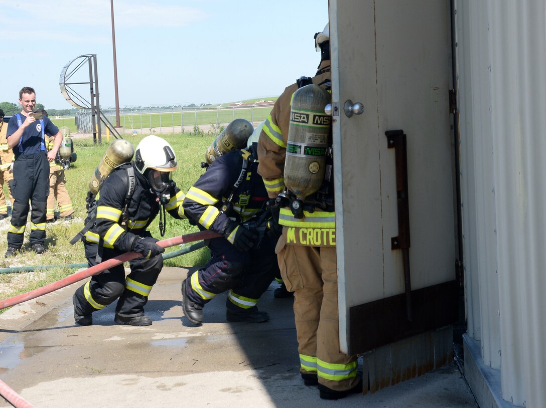 Master Sgt. Matthew Croteau, 155th Air Refueling Wing, Nebraska National Guard assistant fire chief, holds a door open for firefighters from the Czech Republic air force during a simulated structural burning at Offutt Air Force Base, Nebraska June 5, 2019. The Nebraska Air National Guard has a collaboration with the Czech Republic through the State Partnership Program. This is the second year the Nebraska ANG and the Czech Republic has participated in the SPP.