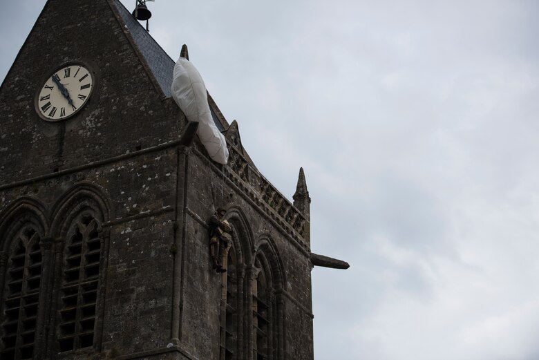 The parachute of the U.S. Army Private John Steele monument billows in the breeze on the Sainte-Mère-Église Church spire in Sainte-Mère-Église, France, June 6, 2019. This year marks the 75th anniversary of D-Day when U.S. forces stormed the beaches of Normandy, France. During this invasion, Steele dropped from the skies with infrantrymen belonging to the 82nd Airborne Division with the objective of seizing Sainte-Mère-Église from Axis defenses. During the drop, Steele’s parachute snagged on the church tower where he pretended to be dead for two hours before Germans took him prisoner. Four days later he escaped captivity and rejoined his division. Steele was awarded the Bronze Star for valor and the Purple Heart for wounds sustained in combat. (U.S. Air Force photo by Senior Airman Kristof J. Rixmann)