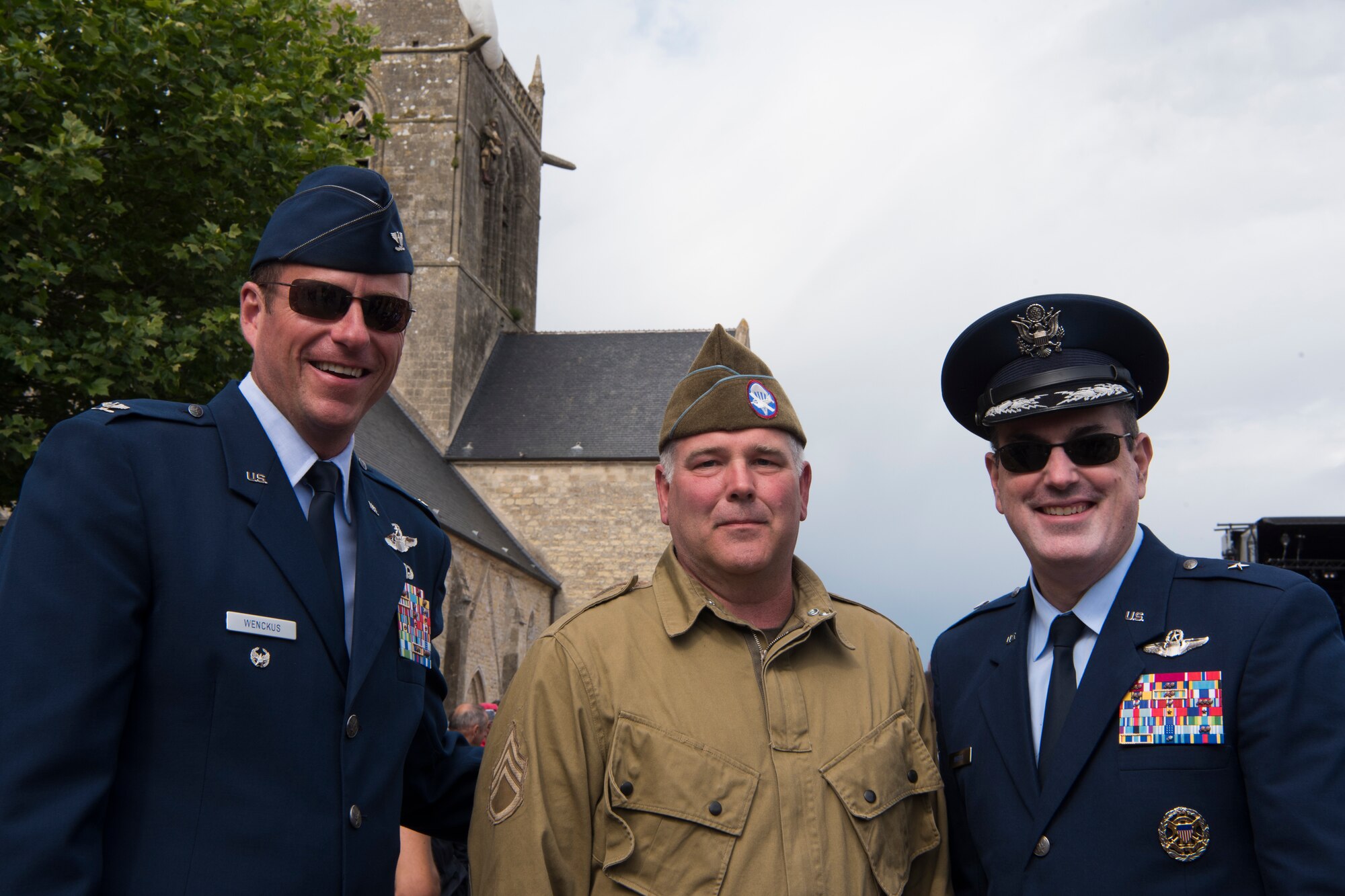 U.S. Air Force Brig. Gen. Mark August, 86th Airlift Wing commander, and Col. Joseph Wenckus, 86th Airlift Wing vice commander, pose with a U.S. military veteran dressed in a WWII-era uniform in honor of the 75th anniversary of D-Day in Sainte-Mère-Église, France, June 6, 2019. Behind them is the church of which U.S. Army Private John Steele’s parachute snagged on the tower during the D-Day invasion. Steele would be captured by German forces but would escape captivity four days later and return with the 82nd Airborne Division. (U.S. Air Force photo by Senior Airman Kristof J. Rixmann)