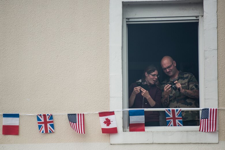 Two French locals, from their second story apartment, compare photos of the crowds gathered in the village square in Sainte-Mère-Église, France, June 6, 2019. To commemorate the 75th anniversary of D-Day, the village square was filled with events ranging from an 82nd Airborne ceremony to several C-130J Super Hercules flyovers. (U.S. Air Force photo by Senior Airman Kristof J. Rixmann)