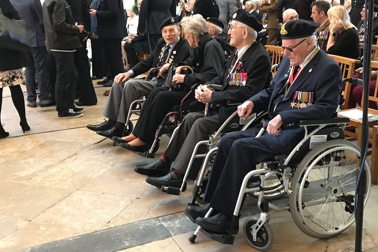 Four elderly men sitting in wheelchairs wear military medals.