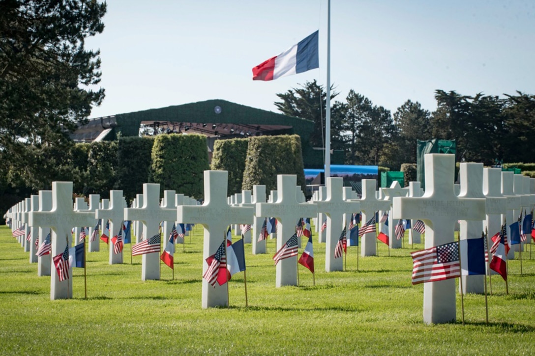 White crosses and small country flags mark graves in a cemetery.