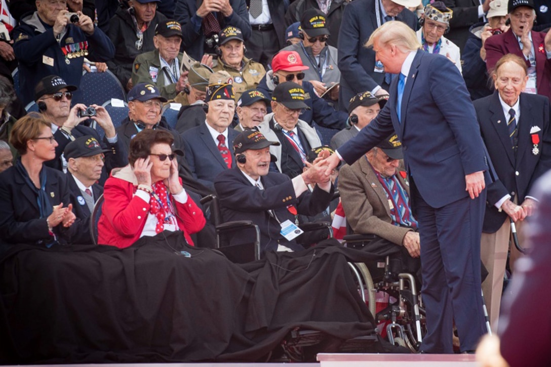 President Donald J. Trump shakes hands with a WWII veteran who is sitting in a wheelchair.