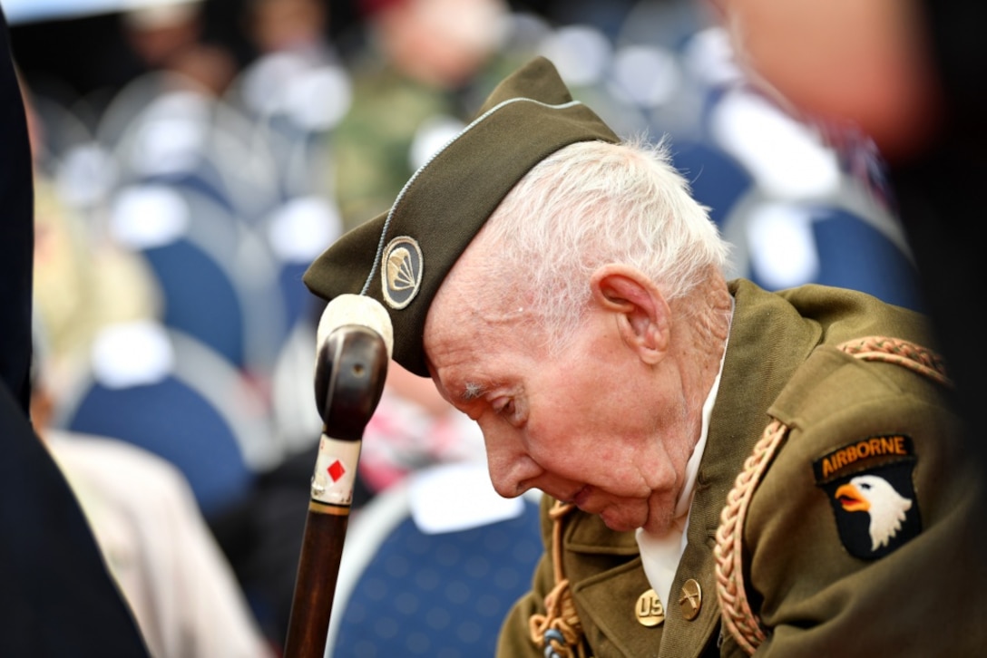 An elderly man wearing a military uniform hangs his head during a ceremony.